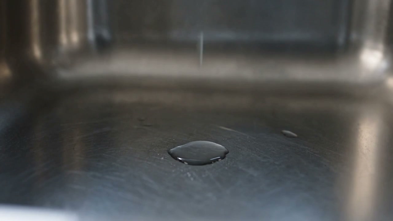 A puddle of water catching low light in the base of a stainless steel sink